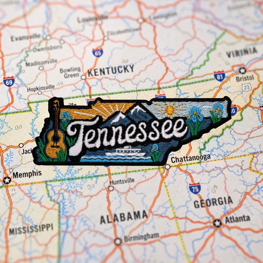 Tennessee embroidered patch – state-shaped design with bold Tennessee lettering, mountain landscape, guitar, riverboat, and floral details